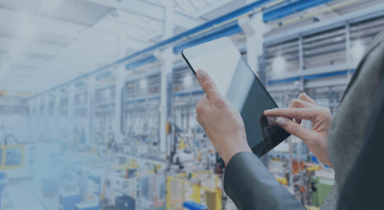 Woman holding a tablet overlooking a manufacturing plant floor